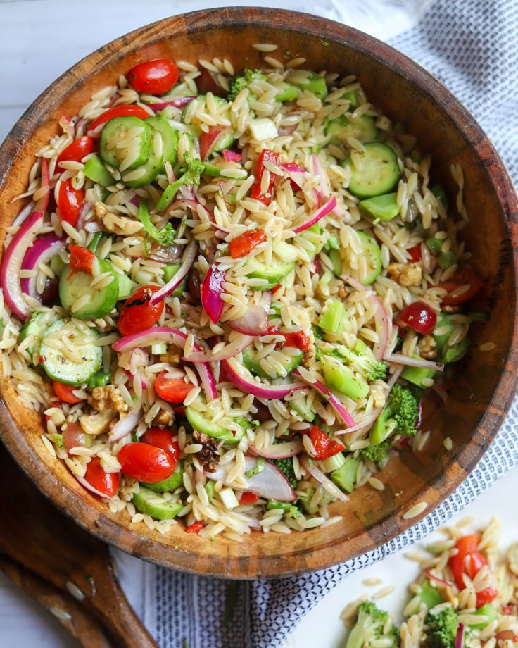 a wooden bowl filled with pasta salad and veggies on top of a table