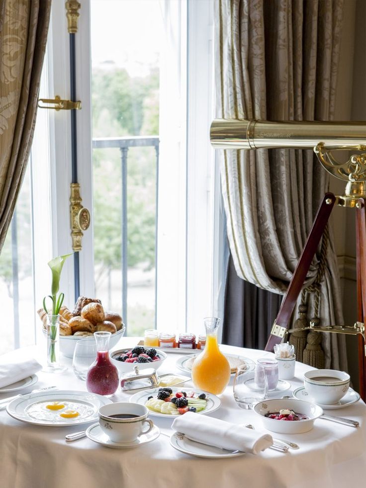 the table is set with food and drinks for two people to enjoy in front of an open window