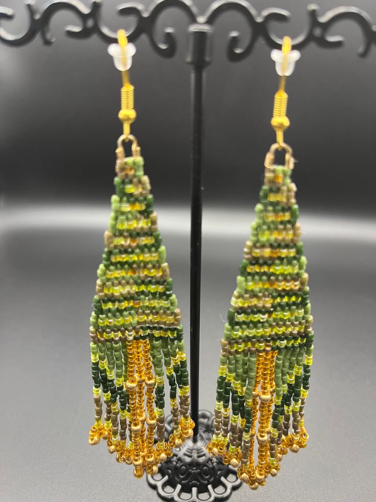 "The woods are calling and this earring is listening. Forest fantasy vibes with rich green hues and deep golden accents. Gold-tone findings and glass seed beads - 5\" long" Green Beaded Bohemian Chandelier Earrings, Green Bohemian Chandelier Earrings With Dangling Beads, Bohemian Green Beaded Chandelier Earrings, Green Bohemian Beaded Dangle Earrings, Bohemian Green Chandelier Earrings With Ear Wire, Green Beaded Earrings With Round Beads, Green Festival Earrings, Bohemian Green Chandelier Earrings With Colorful Beads, Green Bohemian Chandelier Earrings With Colorful Beads