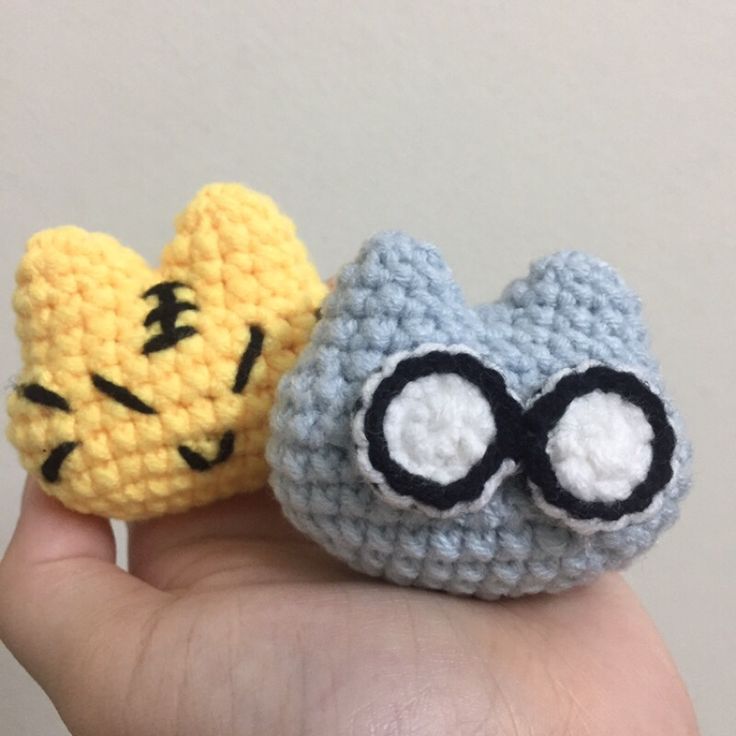 two small crocheted items are sitting on someone's hand, one is yellow and the other is blue