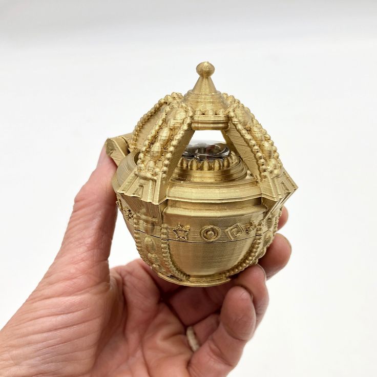 a hand holding a small gold object in it's right hand, with the lid open