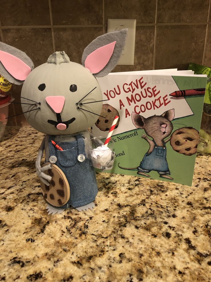 a mouse holding a cookie next to a book on a kitchen counter with chocolate chip cookies