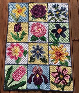 a crocheted blanket with flowers on it sitting on a wooden floor in front of a wood floor