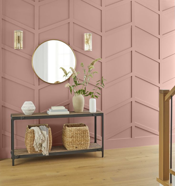 a living room with pink walls and wooden flooring in the background, there is a shelf with baskets on it next to a mirror