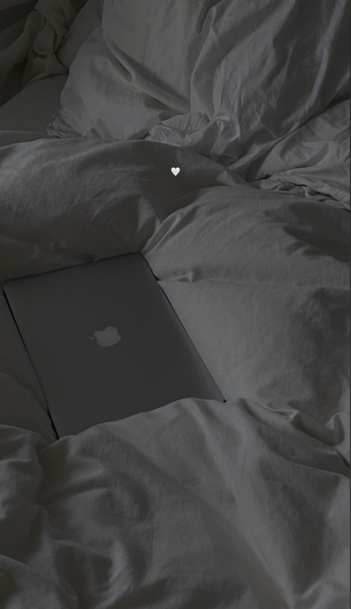 an apple laptop sitting on top of a bed covered in white sheets and blankets,