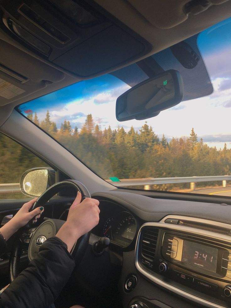 a person driving a car on a highway with trees in the background and clouds in the sky