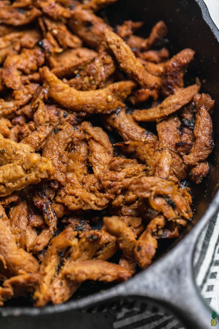 chicken is cooking in a skillet on top of a table with utensils