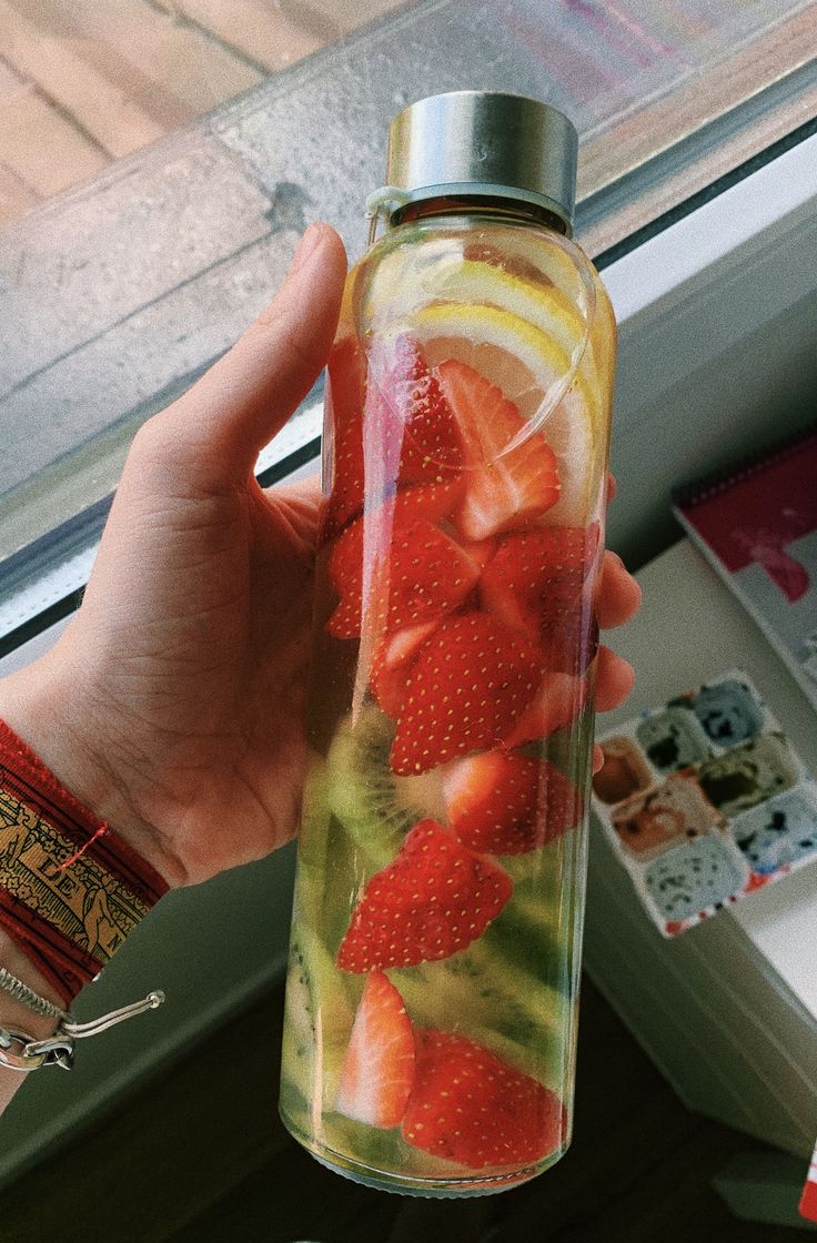 a person holding up a glass bottle filled with liquid and strawberries on the inside