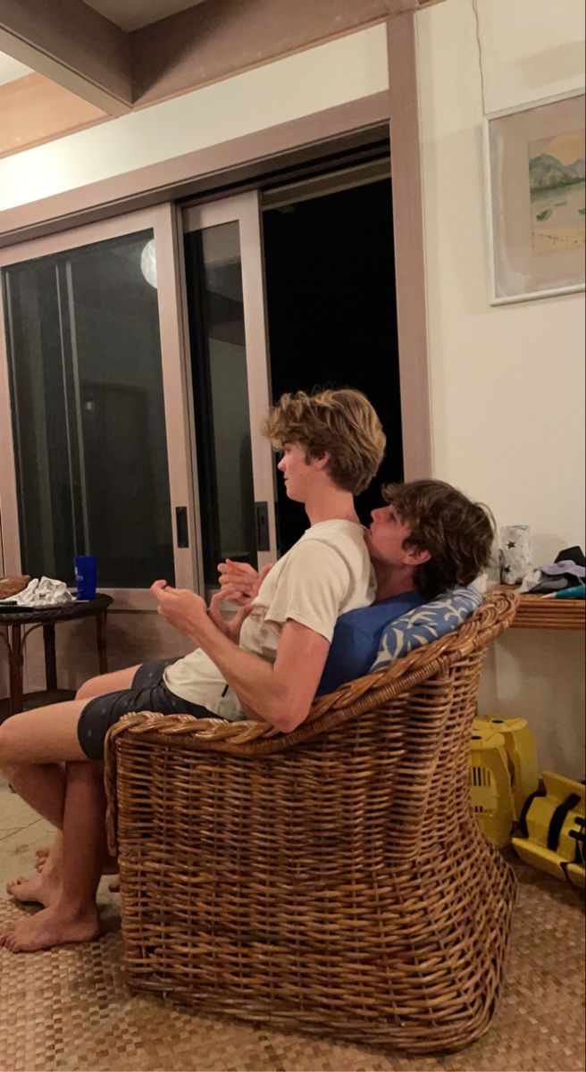 two people sitting on a wicker chair in front of a sliding glass door,