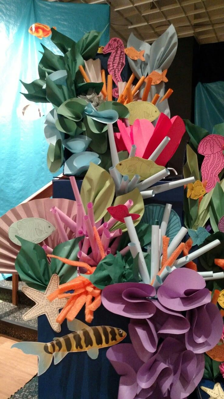 an arrangement of colorful paper flowers in a vase on a table next to a blue wall