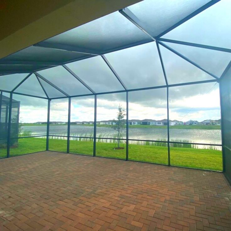 the inside of a building with glass walls and brick flooring, overlooking a body of water