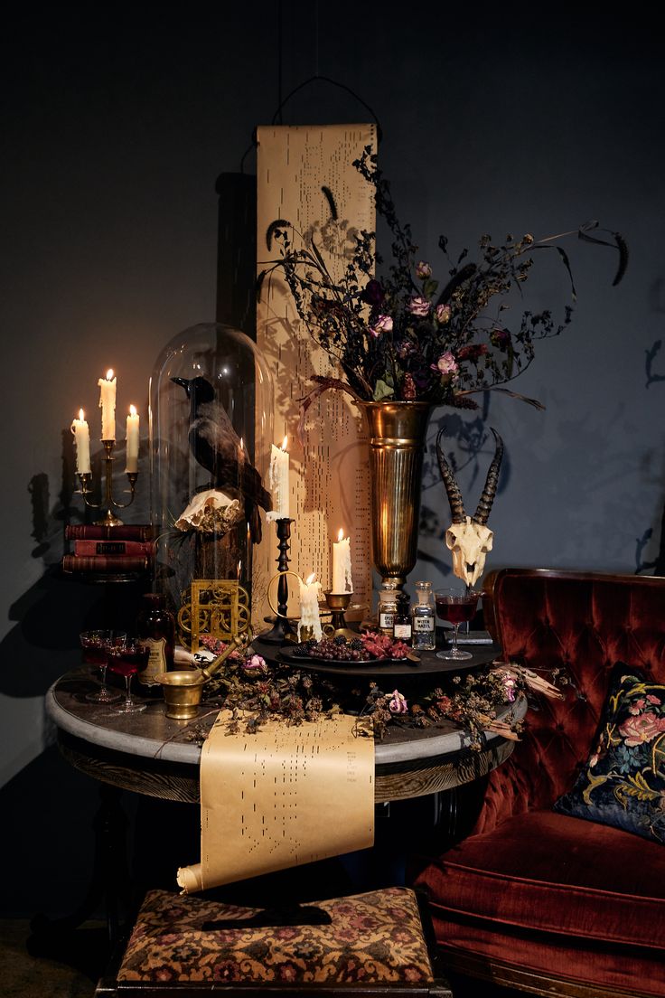 a table topped with candles and vases next to a red velvet chair on top of a wooden floor