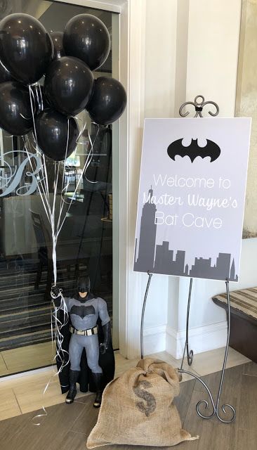 a welcome sign with balloons and a batman figure next to it