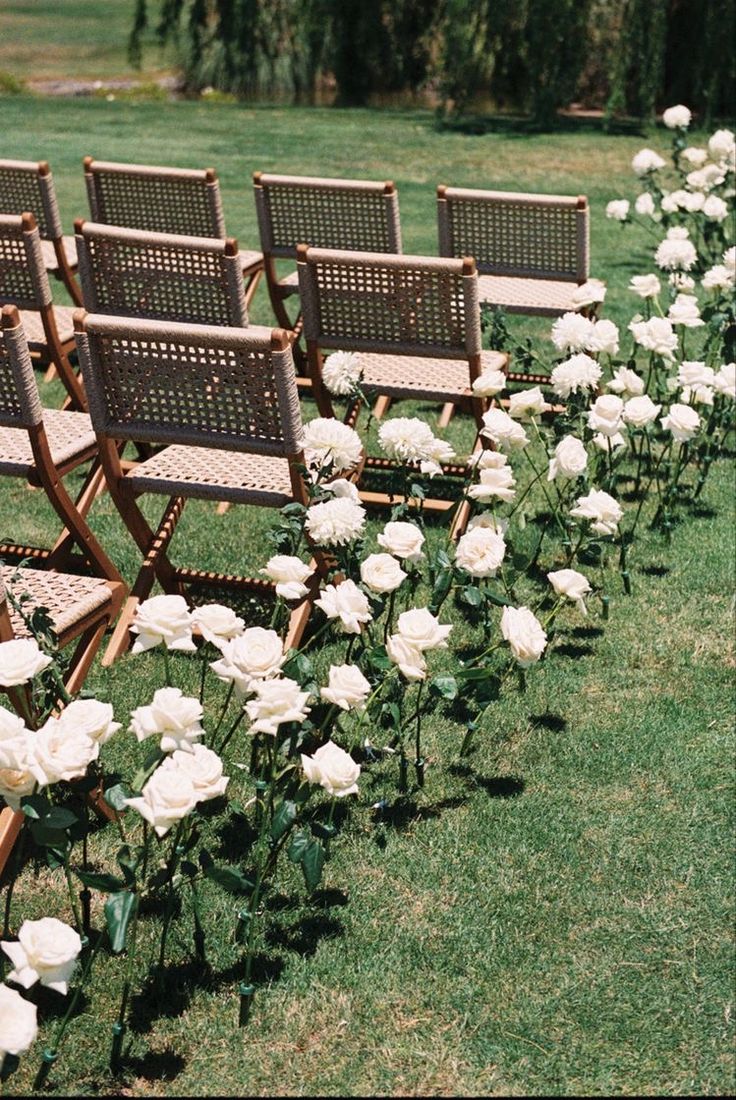 rows of chairs lined up in the grass with white flowers on each chair and one row of them