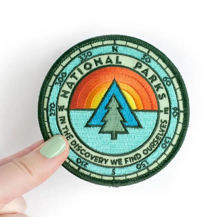 someone is holding up a patch with the national park logo on it and there are two fingers pointing at it