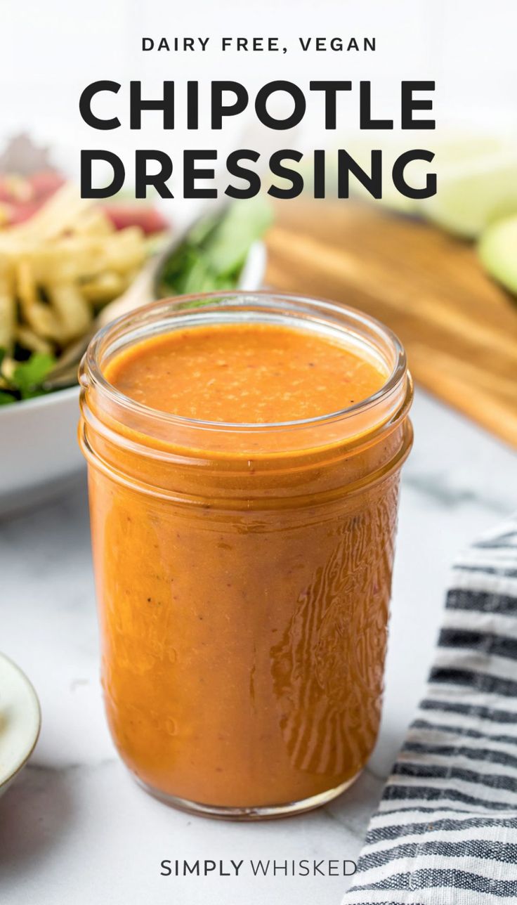 a glass jar filled with chipotle dressing next to a bowl of salad on a table