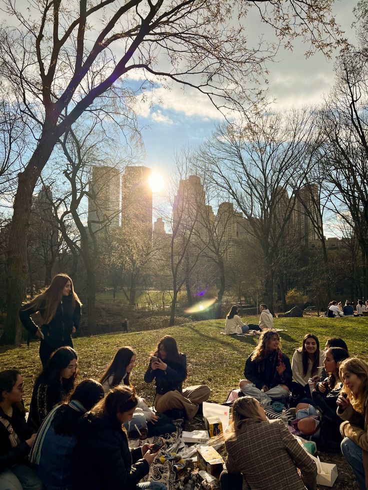 a group of people sitting on top of a lush green field next to a park