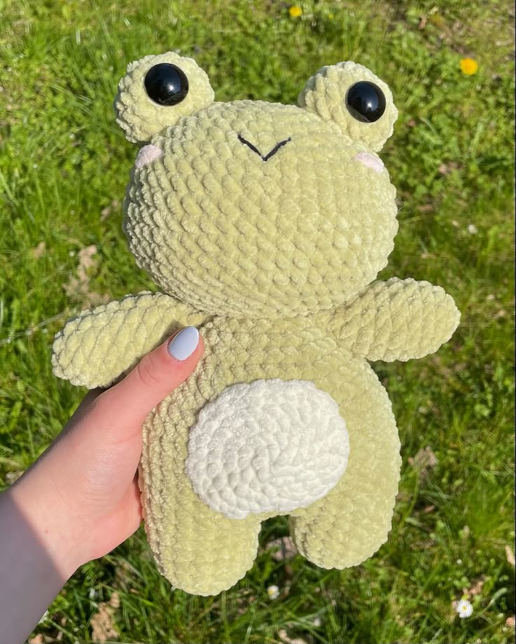 a hand holding a small stuffed animal in the grass