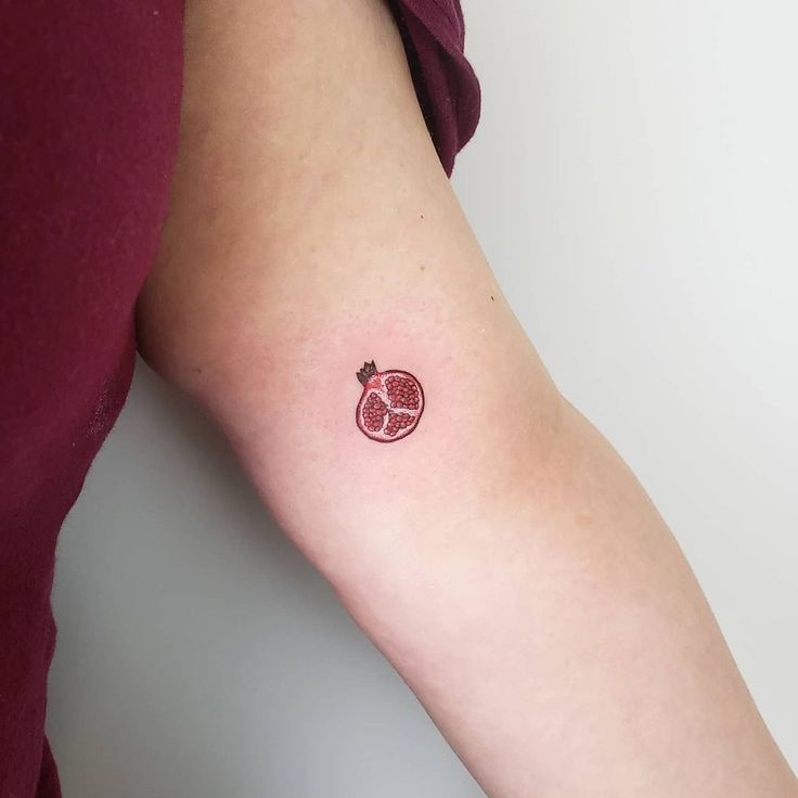 a person with a red apple and pomegranate tattoo on their left arm