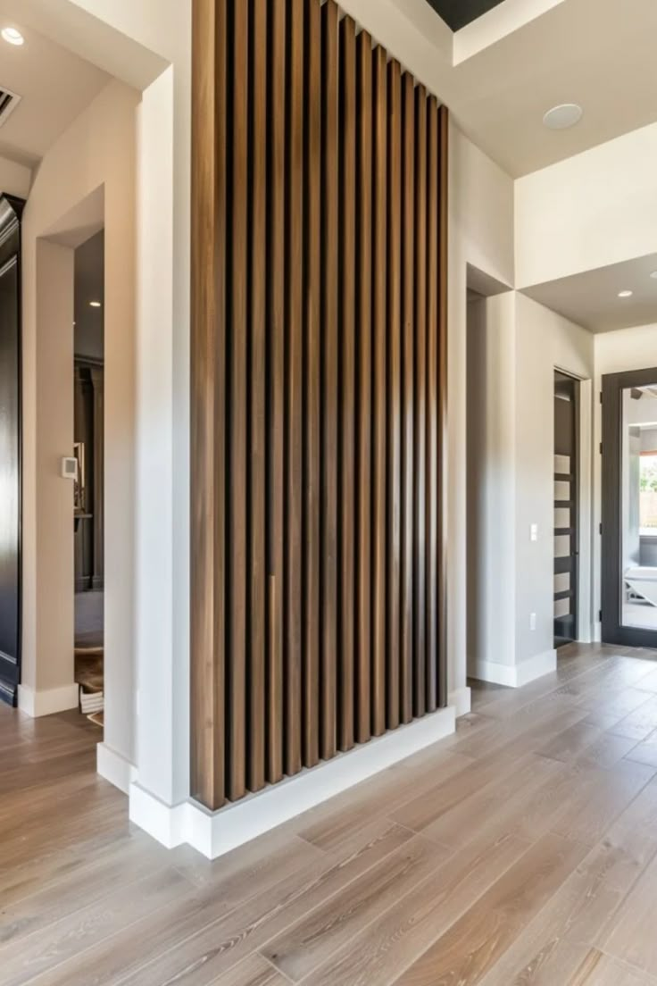 Modern home interior showcasing a wooden slatted room divider integrating with a structural column, against a backdrop of light hardwood floors and white walls. Bedroom Accent Wall Wood Trim, Entry Way Feature Wall Ideas, Wood Accents In Home, Accent Wall Vertical, Wood Wall Accent Ideas, Slat Wall Ideas Living Room, Slat Wall Living Room, Wood Slats Accent Wall, Wood Slat Tv Wall