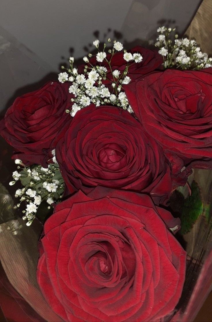 a bunch of red roses sitting in a vase with baby's breath on it