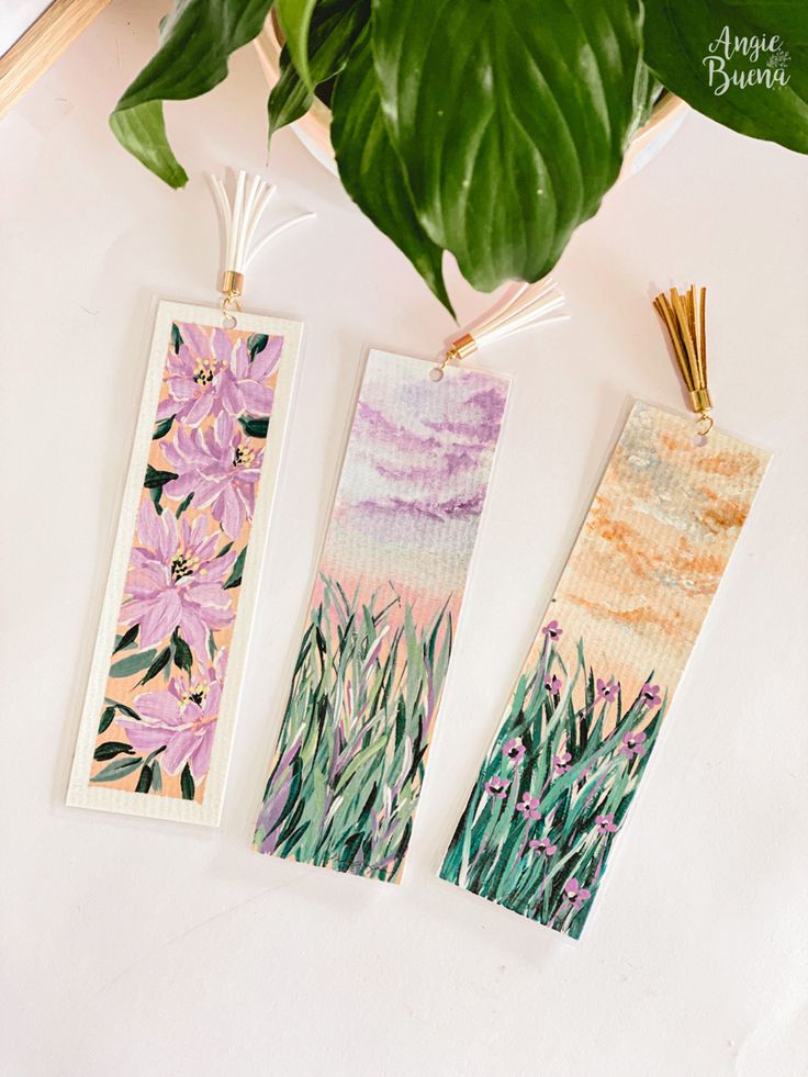 three bookmarks with purple flowers on them next to a potted plant and other items