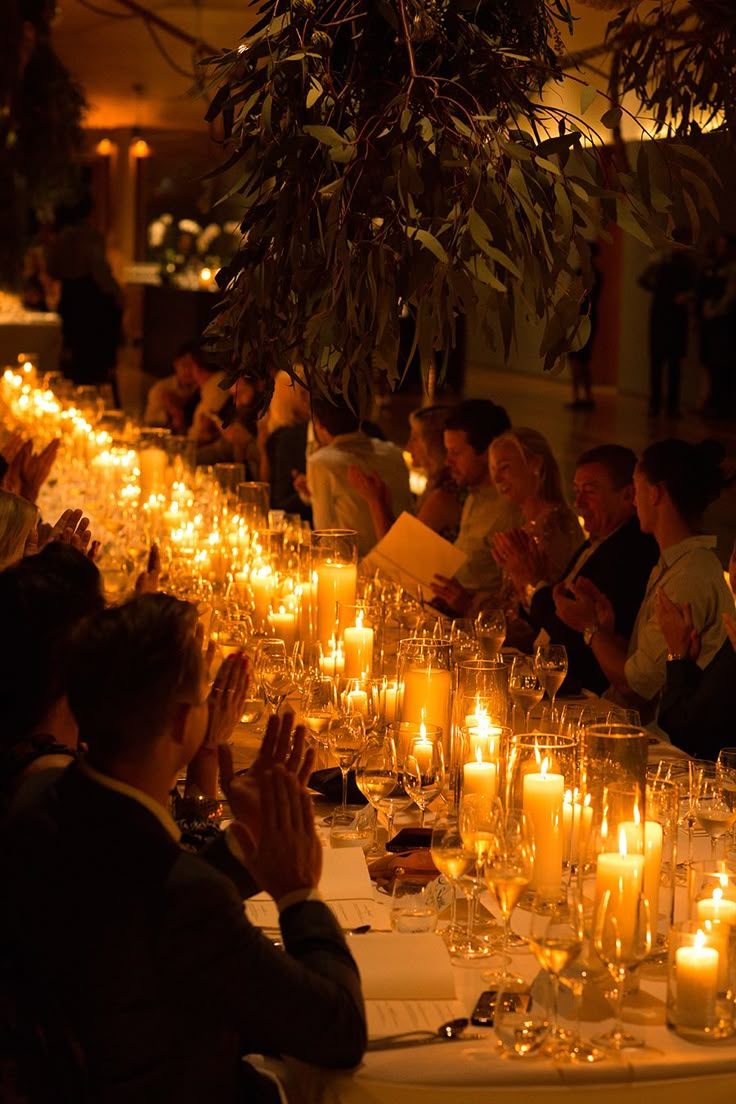 many people are sitting at a long table with candles