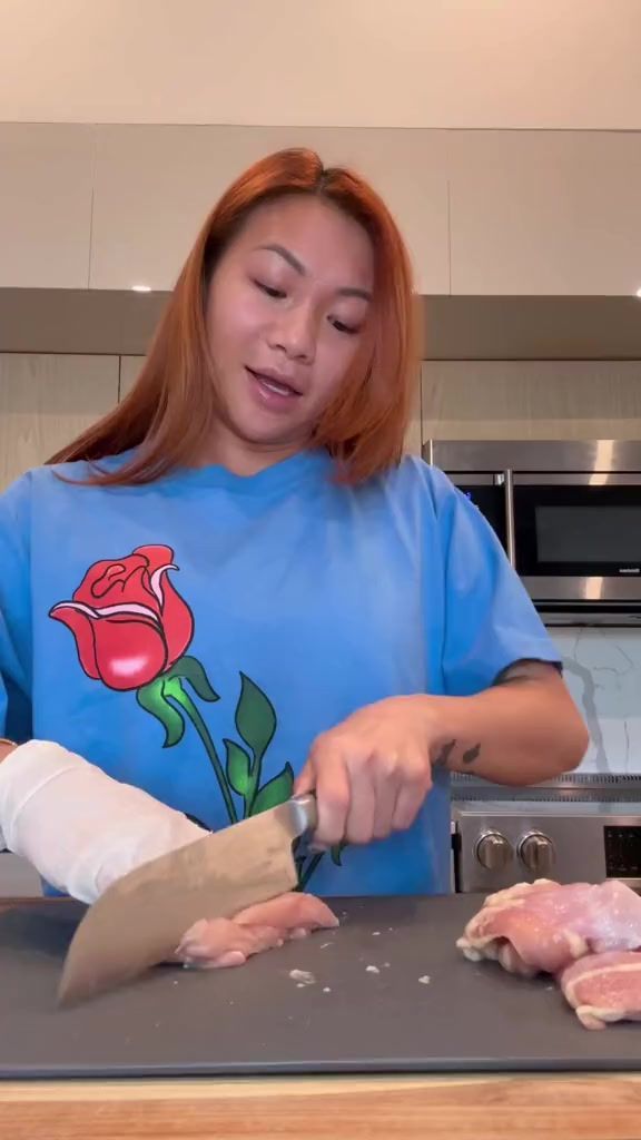 a woman cutting up meat on top of a counter next to a knife and glove