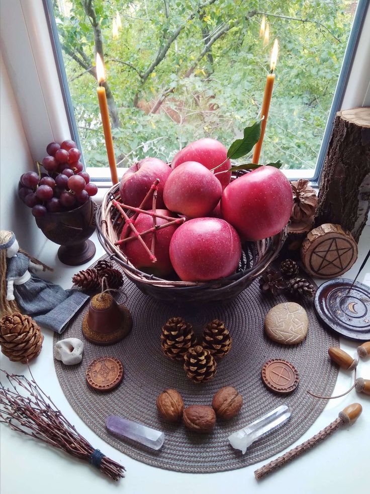 a bowl filled with apples sitting on top of a table next to candles and other items