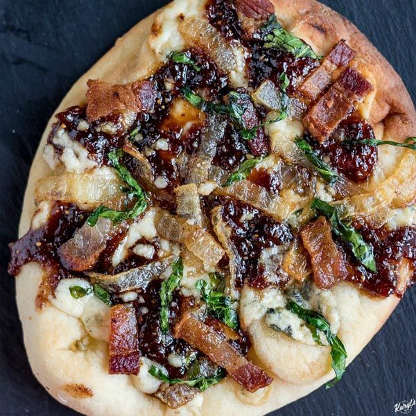 a pizza with bacon, spinach and cheese on it sitting on a black surface