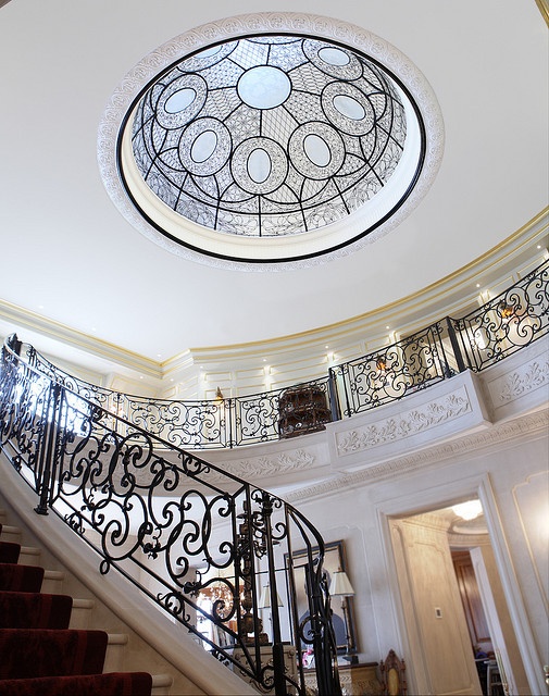 an ornate stair case in the middle of a room with a circular glass window above it