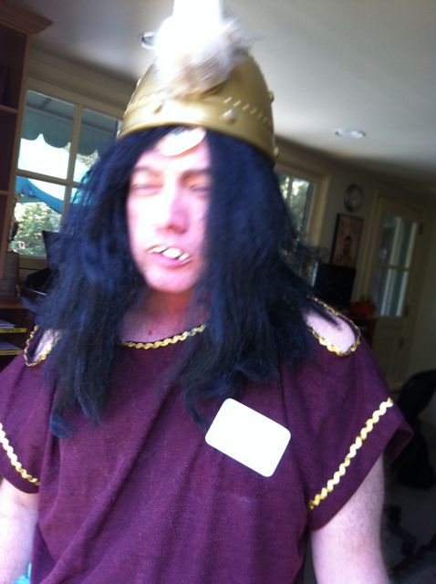 a man with long black hair wearing a purple shirt and a gold crown on his head