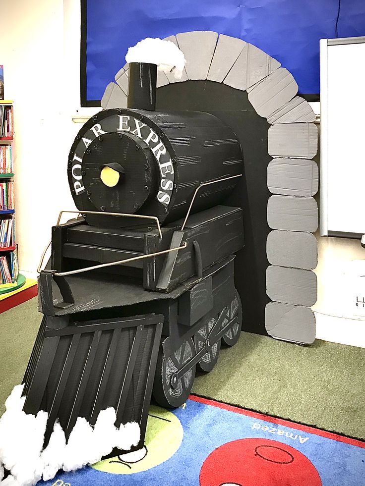 a train made out of cardboard sitting on top of a floor next to a book shelf