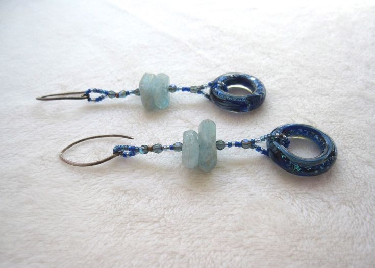 These ocean colored stones will give off some serious mermaid vibes! Like the sea itself, this pair of earrings is fluid! They can easily be worn with day or night looks. Radiant hand made glass rings suspend below exquisite aquamarine stones. Sterling silver ear wires. 2 1/2" long. Nickel-free Blue Aquamarine Jewelry, Handmade Turquoise Aquamarine Earrings, Blue Recycled Glass Dangle Earrings, Aquamarine Dangle Earrings With Ear Wire, Blue Long Drop Wire Wrapped Jewelry, Aquamarine Drop Earrings With Ear Wire, Turquoise Glass Drop Earrings, Handmade Aquamarine Dangle Earrings, Nickel Free Blue Aquamarine Earrings