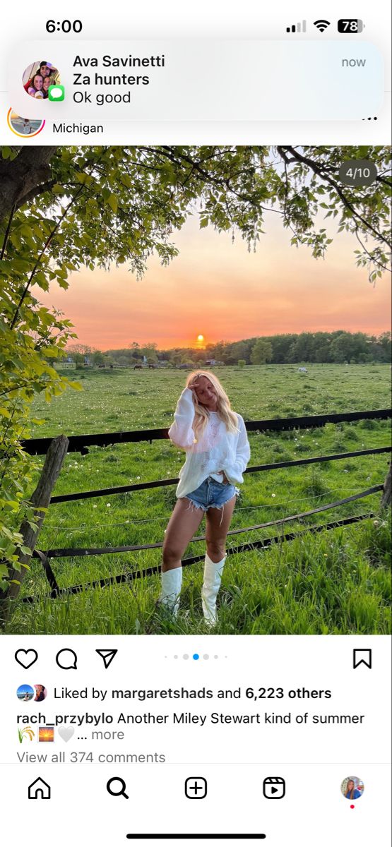 a woman in white shirt and shorts standing next to a fence with trees on it