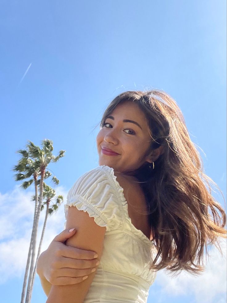 a woman standing in front of palm trees with her arms around her body and smiling