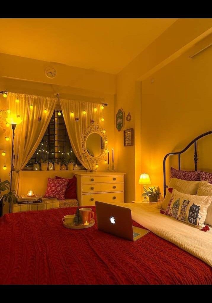 a laptop computer sitting on top of a red bed in a room with yellow walls