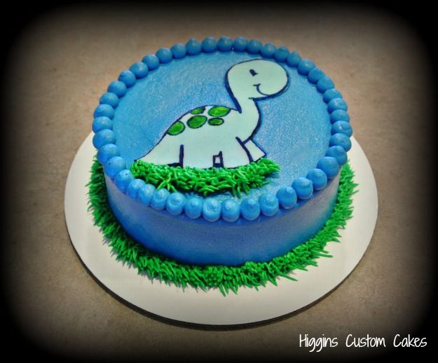 a birthday cake decorated with an image of a dinosaur on the front and green grass around it