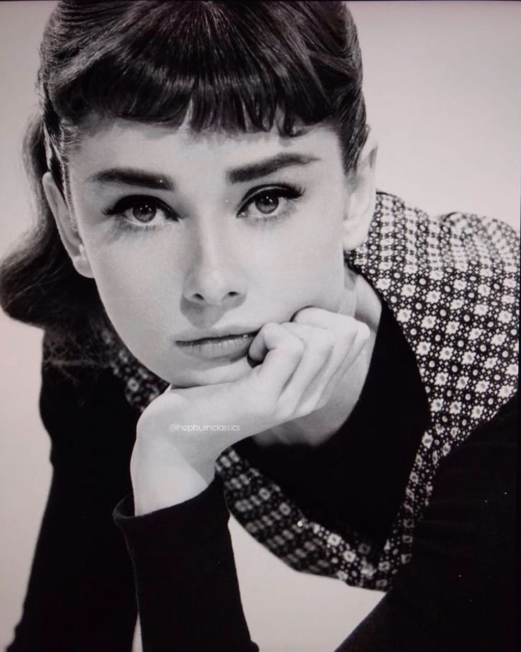 a black and white photo of a woman with her hand on her chin looking at the camera