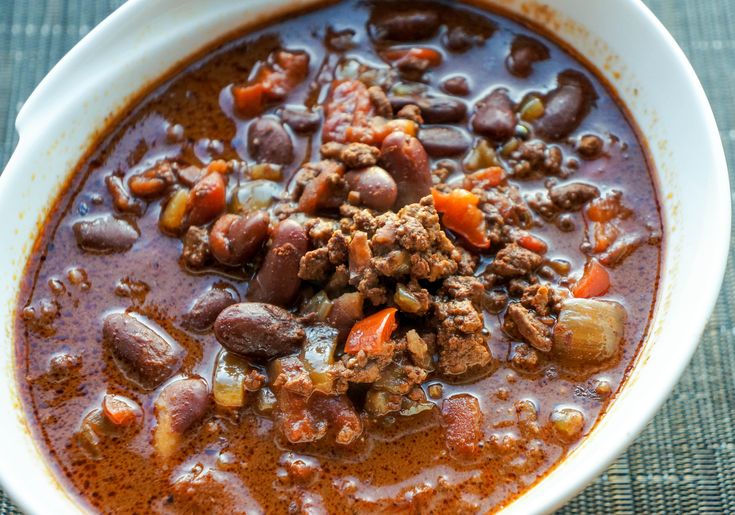 a white bowl filled with chili and meat soup on top of a blue table cloth