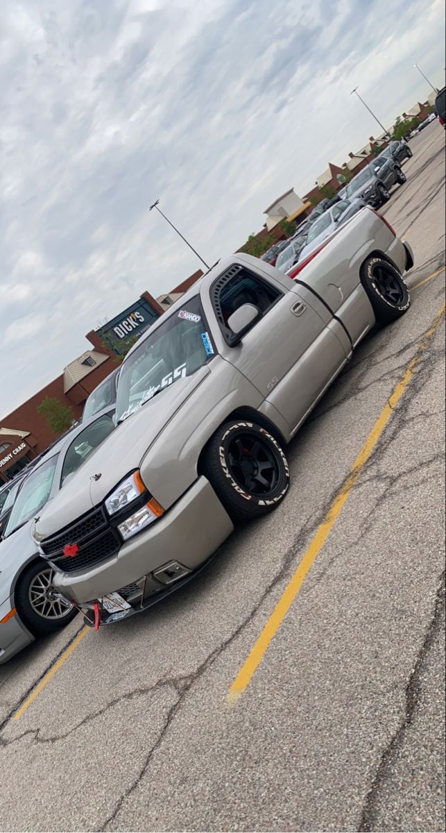 a silver truck parked in a parking lot next to other cars on the side of the road