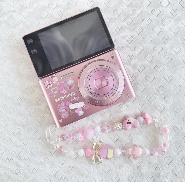 a pink camera sitting on top of a table next to a beaded bracelet and necklace