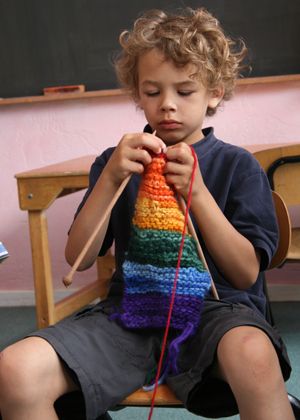 a little boy sitting on a wooden chair while holding a colorful crocheted object