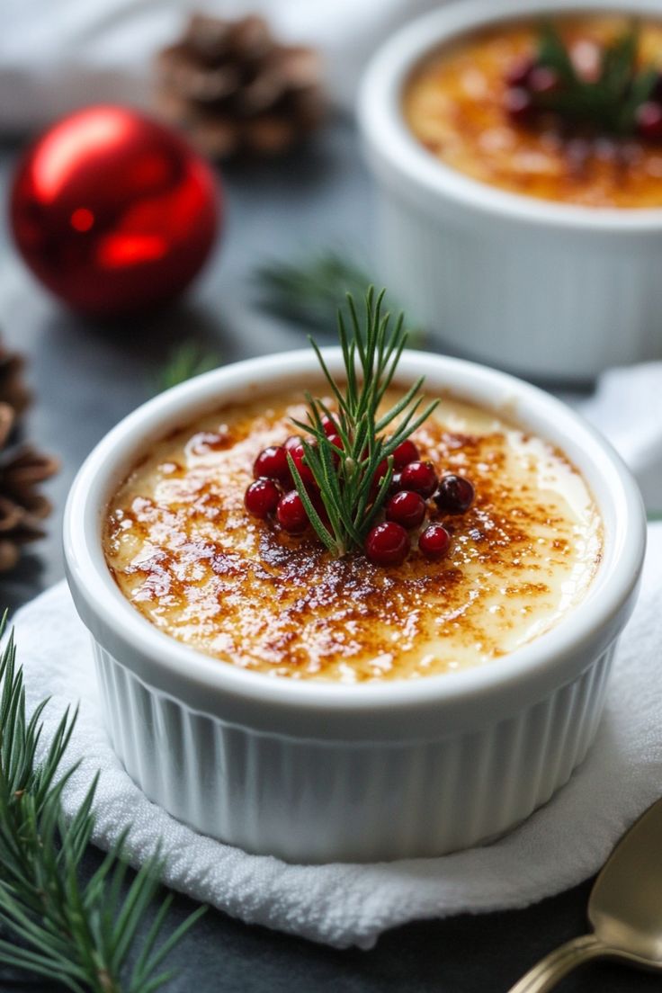 Creme brulee topped with red berries and a sprig of rosemary, surrounded by holiday decorations. Holiday Plated Desserts, Egg Nog Creme Brulee, Christmas Elegant Desserts, Panna Cotta Christmas, Creme Brulee Christmas, Eggnog Creme Brulee Recipe, Holiday Creme Brulee, Christmas Dessert Elegant, Christmas Dessert Fruit