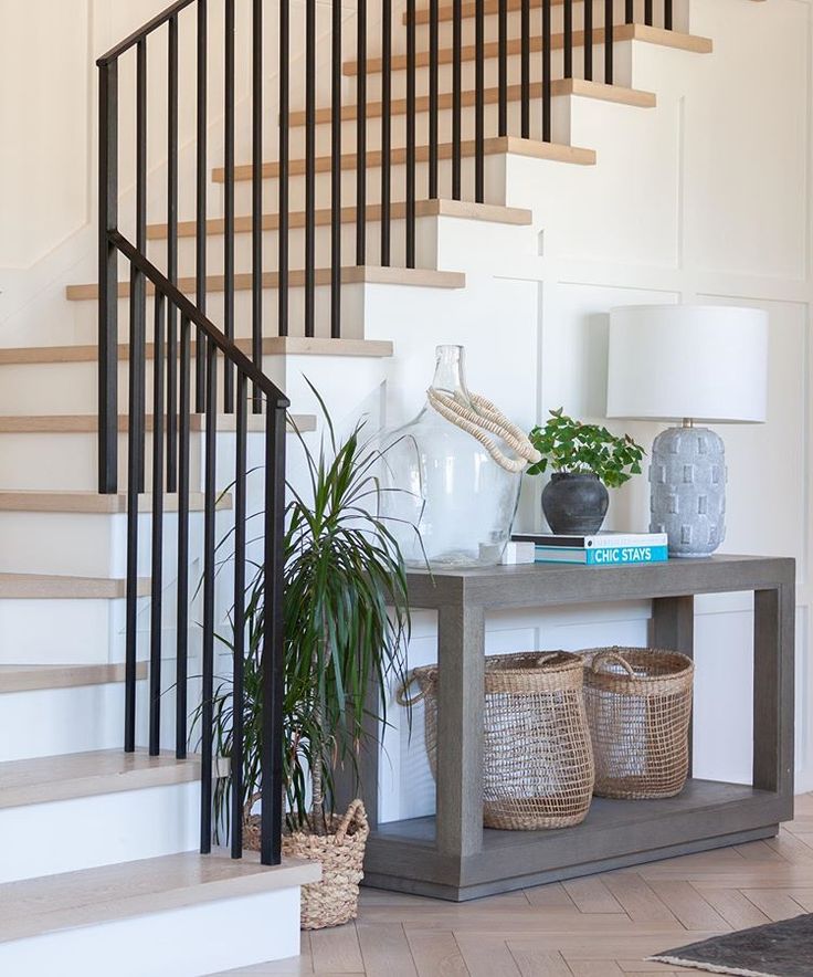 there is a plant on the table in front of the stair case and basket under the banister