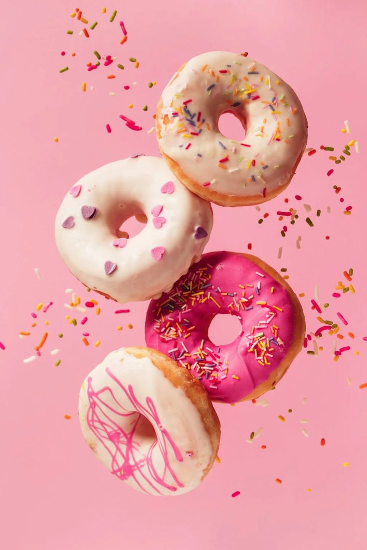 five donuts with sprinkles on a pink background