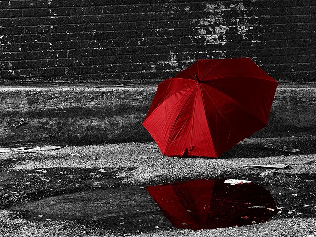 a red umbrella sitting on the ground next to a brick wall with water puddles