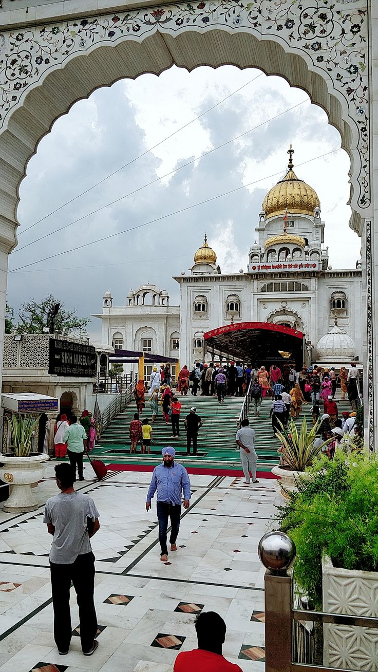 many people are walking around in front of a white building with gold domes on it