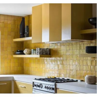 a kitchen with yellow and white tiles on the backsplash, stove top and cabinets