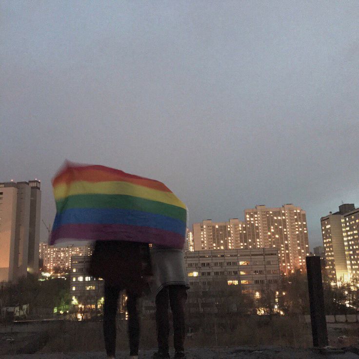 two people standing under an umbrella in front of some tall buildings at night with the city lights behind them